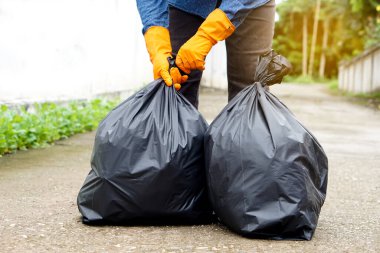 Closeup man holds black plastic bag that contains garbage inside. Concept : Waste management. Environment problems. Daily chores. Throw away rubbish.