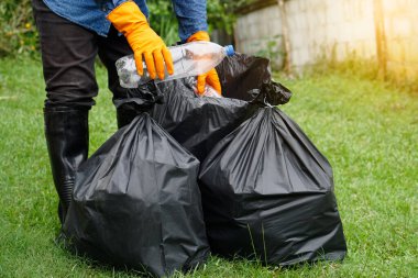 Closeup garbage collector worker hands hold plastic bottles to put into black garbage bags to recycle. Concept : Environment conservation. Waste management. Cleaning public place activity. 