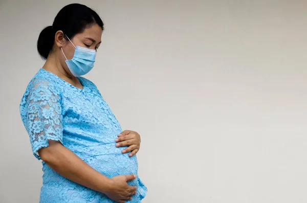 Pregnant Asian woman wears hygienic face mask, holds her big belly, Feels worried. Concept : Depression symptom of pregnant woman in Covid-19 epidemic and bad economic. 9 months pregnancy.