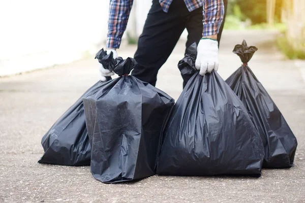 Closeup  man holds black plastic bag that contains garbage inside. Concept : Waste management. Environment problems. Daily chores. Throw away rubbish .