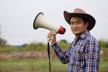 Asyalı adam şapka takıyor, ekose gömlek giyiyor, megafonu tutuyor. Konsept: İletişim, duyuru. İtiraz ediyorum. Protestocu. Dünyaya bir şey duyur. Megafon halka açık adres megafonu.   