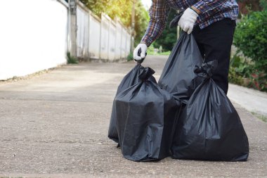 Closeup  man holds black plastic bag that contains garbage inside. Concept : Waste management. Environment problems. Daily chores. Throw away rubbish . 