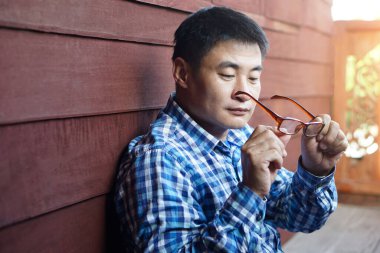 Asyalı orta yaşlı adam lensleri kontrol etmek için gözlük tutuyor. Konsept: görme problemi. Optometri. Dışbükey ya da içe göçük mercekli gözlük. Miyop. Göz hastalığı.  