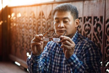 Asyalı orta yaşlı adam lensleri kontrol etmek için gözlük tutuyor. Konsept: görme problemi. Optometri. Dışbükey ya da içe göçük mercekli gözlük. Miyop. Göz hastalığı.  