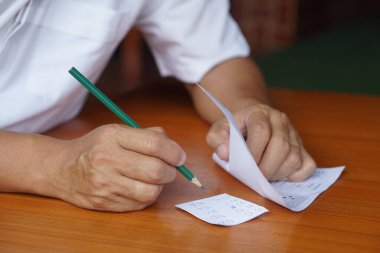 Kapanış öğrencisi kâğıt üzerinde sınav yapıyor ve kağıdın altında cevapları olan küçük bir kağıt parçasını saklıyor. Konsept: Testte hile yapmak. Sahtekâr davranış. Eğitim değerlendirmesi.                