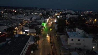 Geceleri dükkanın ışığı ve arabaların hareketi. Kıbrıs, Ayia Napa 'da bir gece. Kamera şehrin üzerinde uçuyor..