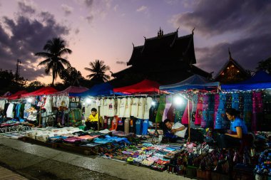 Luang Prabang, Laos - 31 Ocak 2018: Oyalayıcılar Wat Mai Suwannaphumaham tapınağının arkasında güneş batarken cep telefonlarıyla zaman geçiriyorlar