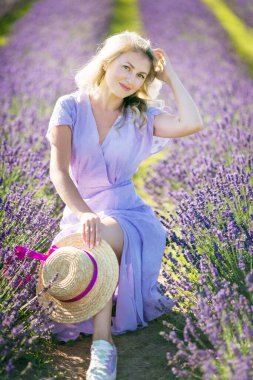 Beautiful blonde smiling woman in violet dress outdoors on lavender field summer day. Girl enjoying journey to travel on vacation, relaxation. aromatherapy. Concept Summer, aromas. Natural cosmetics