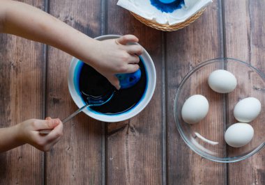 Kız yumurtaları beyaz tabağa boyuyor. Paskalya