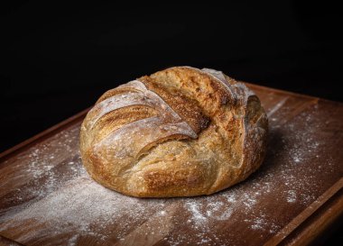 Siyah arkaplanı olan tahtanın üzerinde un tozuna bulanmış taze ekşi ekmek..