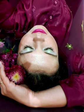 Küvette kasımpatı yaprakları içinde çıplak yatan siyah saçlı seksi güzel bir kadının moda fotoğrafı. Menekşe pembesi içinde güzel bir kız. Kasımpatı dolu bir küvette çok peri suyu.