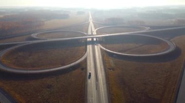 Arabalar çok katlı bir kavşakta ilerliyorlar. Günbatımında güz ağaçlarıyla yol üzerinde uçan insansız hava aracı görüntüsü