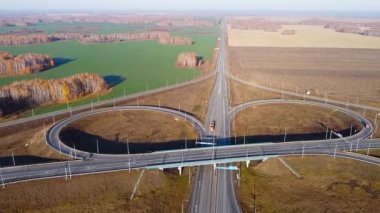 Hareket halindeki arabalarla çok katlı kavşak yolunun hava aracı görüntüsü. Günbatımında düşen ağaçlarla kır yolunda uçan insansız hava aracı görüntüleri.