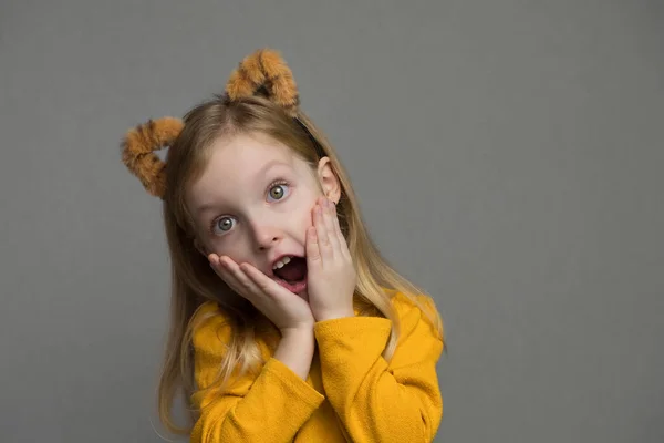 Aranyos szőke lány tigris fülekkel. Egy fejdísz tigris fülekkel. 2022 új éve. A tigris jelmezes gyerek édesen mosolyog és a kamerába néz.. — Stock Fotó