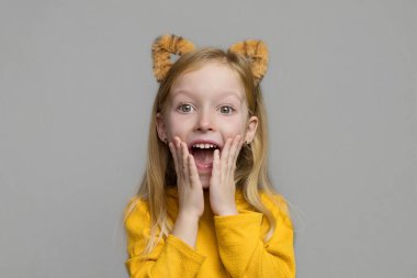 Kaplan kulaklı, sarışın, tatlı, şaşkın bir kız. Kaplan kulaklı bir başlık. Yeni yıl 2022. Kaplan kostümlü çocuk tatlı tatlı gülümser ve kameraya bakar..