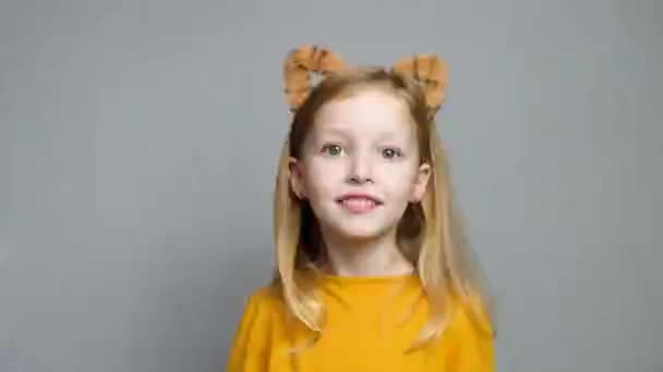 Schattig lachend blond meisje met tijgeroren. Een hoofdtooi met tijgeroren. Nieuwjaar 2022. Kind in een tijger kostuum glimlacht lief en kijkt naar de camera. — Stockvideo