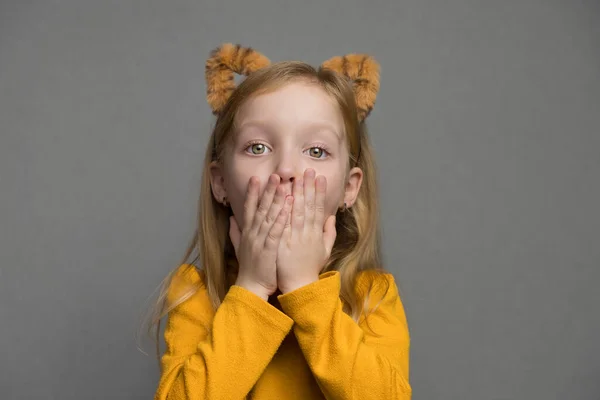Aranyos, meglepett szőke lány tigris fülekkel. Egy fejdísz tigris fülekkel. 2022 új éve. A tigris jelmezes gyerek édesen mosolyog és a kamerába néz.. — Stock Fotó