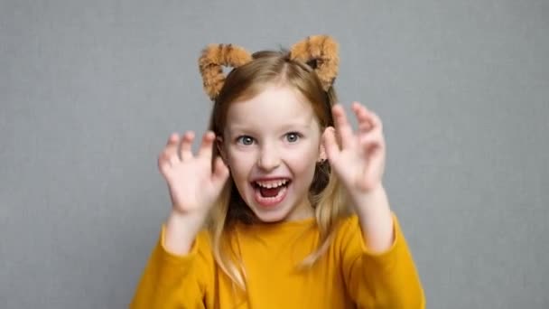 Jolie fille blonde souriante avec des oreilles de tigre. Une coiffe avec des oreilles de tigre. Nouvel An 2022. Enfant dans un costume de tigre sourit doucement et regarde la caméra. — Video