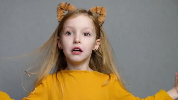 Χαριτωμένο ξανθό κορίτσι με αυτιά τίγρης. Φόρεμα κεφαλής με αυτιά τίγρης. Νέο έτος 2022. Ένα παιδί με στολή τίγρης χαμογελάει γλυκά και κοιτάζει την κάμερα. — Αρχείο Βίντεο