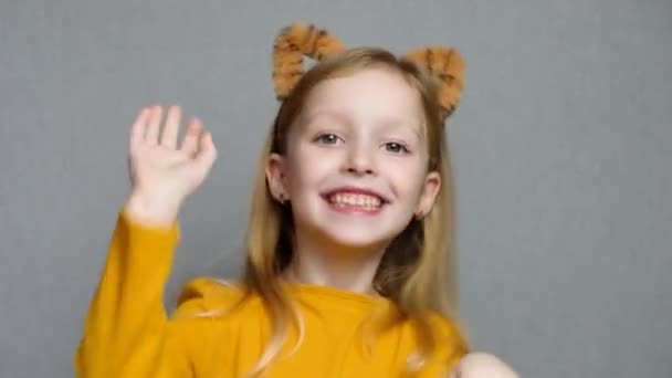 Aranyos mosolygós szőke lány tigris fülekkel. Egy fejdísz tigris fülekkel. 2022 új éve. A tigris jelmezes gyerek édesen mosolyog és a kamerába néz.. — Stock videók