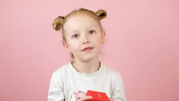 핑크 배경에 빨간 선물 상자를 흔들며 웃고 있는 이상 한 금발 소녀. 발렌타인데이 또는 어머니 날의 개념 — 비디오