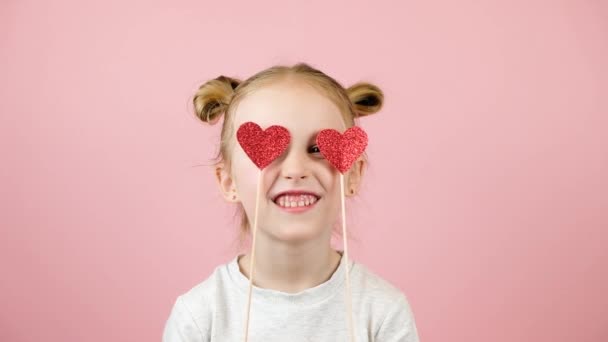 Divertente bambina bionda sorridente e giocando con il giocattolo del cuore rosso su sfondo rosa. Concetto di San Valentino o Festa della Mamma — Video Stock