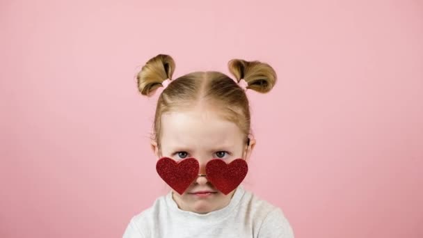 Kırmızı kalpli komik küçük sarışın kız pembe arka planda güneş gözlüğü şeklinde. Sevgililer Günü ya da Anneler Günü konsepti — Stok video