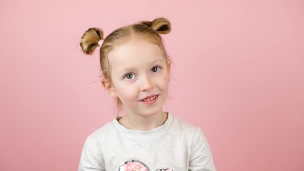 Roligt nyfiken liten blond flicka ler och skakar den röda presentförpackning på rosa bakgrund. Alla hjärtans dag eller mors dag koncept — Stockvideo