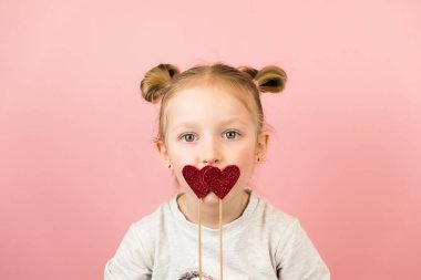 Gülen ve pembe arka planda kırmızı kalp oyuncağıyla oynayan komik sarışın kız. Sevgililer Günü ya da Anneler Günü konsepti