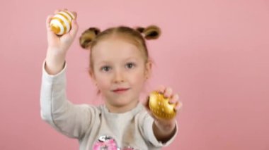 Gülümseyen ve pembe arka planda altın paskalya yumurtalarıyla oynayan komik sarışın kız. Mutlu Paskalyalar