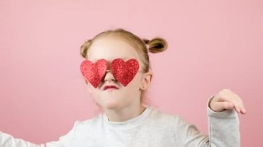 Kırmızı kalp şeklinde gözlüklerle pembe arka planda gülümseyen ve dans eden komik sarışın kız. Sevgililer Günü ya da Anneler Günü konsepti