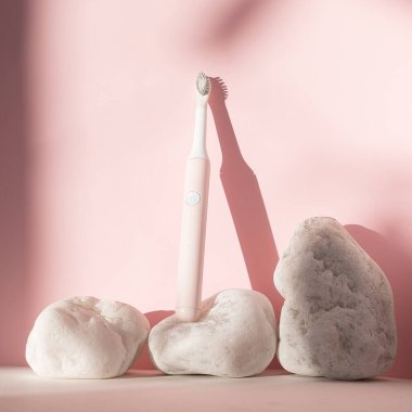 Yeni modern ultrasonik diş fırçası. Pembe pastel arka planda beyaz taşlı diş bakımı malzemeleri. Ağız temizliği, diş ve diş sağlığı, sağlıklı dişler. Diş ürünleri Ultrasonik titreşim diş fırçası.