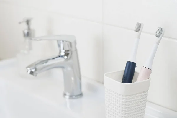 New modern ultrasonic toothbrushes in a glass on the bathroom sink. Jaw model and dental care supplies. Oral hygiene, dental and gum health, healthy teeth. Dental products