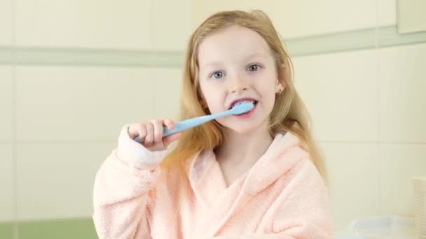 Счастливая улыбающаяся маленькая девочка чистит зубы с помощью ультразвуковой электрической зубной щетки в ванной комнате дома. Гигиена полости рта, здоровье зубов и десен, здоровые зубы. Ежедневная жизнь. — стоковое видео
