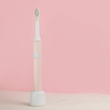 Yeni modern ultrasonik diş fırçaları. Pembe pastel arka planda yeşil yapraklı diş bakımı malzemeleri. Ağız temizliği, sakız sağlığı, sağlıklı dişler. Diş ürünleri Ultrasonik titreşim diş fırçası.