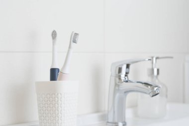 Yeni modern ultrasonik diş fırçaları banyo lavabosundaki bardakta. Çene modeli ve diş bakımı malzemeleri. Ağız temizliği, diş ve diş sağlığı, sağlıklı dişler. Diş ürünleri