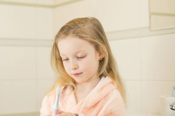 Feliz niña sonriente cepillo de dientes utilizando ultrasónico cepillo de dientes eléctrico en el baño en casa. Higiene bucal, salud dental y de las encías, dientes sanos. Vida diaria y rutina. —  Fotos de Stock