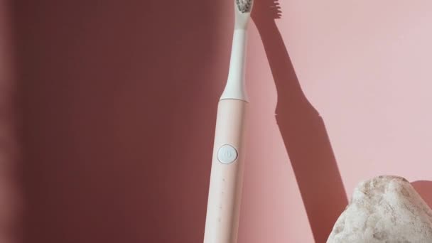 新しい現代の超音波歯ブラシ。ピンクのパステルを背景に顎モデルと歯科ケア用品。口腔衛生、歯科および歯茎の健康、健康な歯。歯科製品｜超音波振動歯ブラシ. — ストック動画