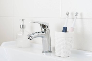 Yeni modern ultrasonik diş fırçaları banyo lavabosundaki bardakta. Çene modeli ve diş bakımı malzemeleri. Ağız temizliği, diş ve diş sağlığı, sağlıklı dişler. Diş ürünleri