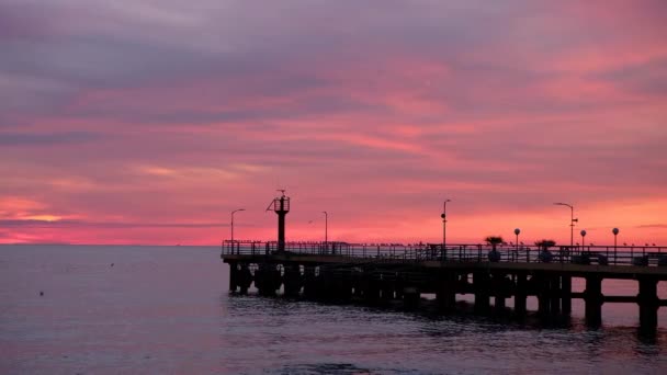 Fishing pier on the ocean with a colorful and golden sunset. Ocean beach sunrise and dramatic colorful sky clouds. — Wideo stockowe