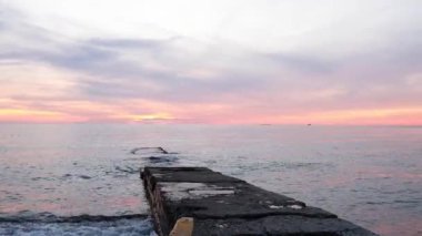 Fishing pier on the ocean with a colorful and golden sunset. Ocean beach sunrise and dramatic colorful sky clouds.
