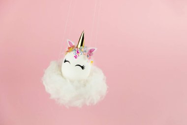 Easter unicorn egg flying on cloud on pastel pink background. Happy easter banner. Kids activity inspiration. Greeting card or poster. Copy space for text. Levitation egg