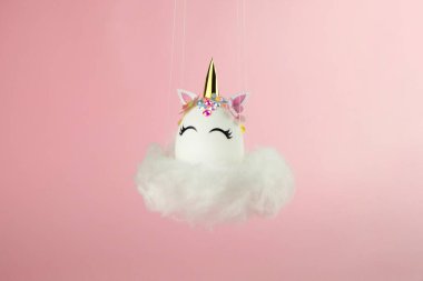 Easter unicorn egg flying on cloud on pastel pink background. Happy easter banner. Kids activity inspiration. Greeting card or poster. Copy space for text. Levitation egg