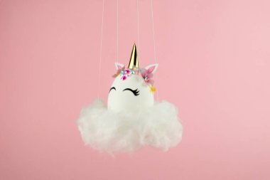 Easter unicorn egg flying on cloud on pastel pink background. Happy easter banner. Kids activity inspiration. Greeting card or poster. Copy space for text. Levitation egg