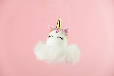 Easter unicorn egg flying on cloud on pastel pink background. Happy easter banner. Kids activity inspiration. Greeting card or poster. Copy space for text. Levitation egg