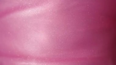 Glittering abstract pink background. Color fluid is swirling in beautiful silver clouds. Glitter dust is moving slowly in water. Amazing abstract texture background.
