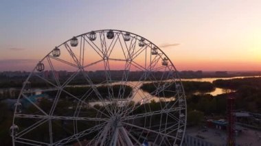 Ferris wheel against a sunset sky. Twilight waves against classic illuminated ferris wheel, amusement park for tourists. Summertime symbol.