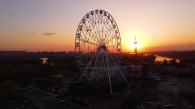 Ferris wheel against a sunset sky. Twilight waves against classic illuminated ferris wheel, amusement park for tourists. Summertime symbol.