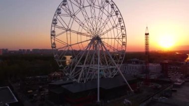 Ferris wheel against a sunset sky. Twilight waves against classic illuminated ferris wheel, amusement park for tourists. Summertime symbol.