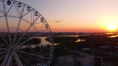 Ferris wheel against a sunset sky. Twilight waves against classic illuminated ferris wheel, amusement park for tourists. Summertime symbol.